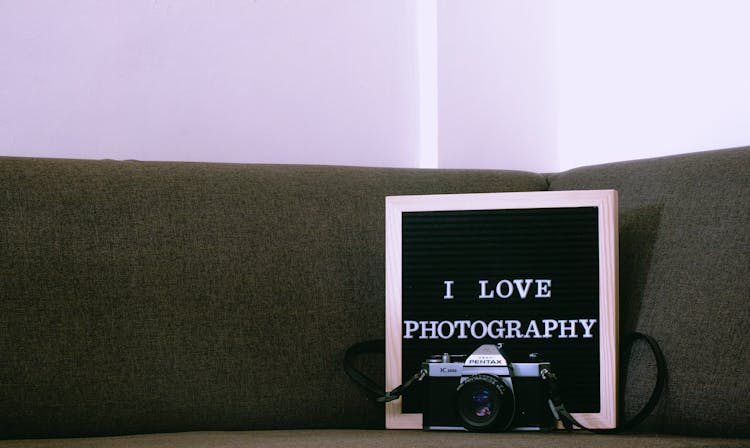 A Letter Board And A Pentax Camera On A Brown Couch