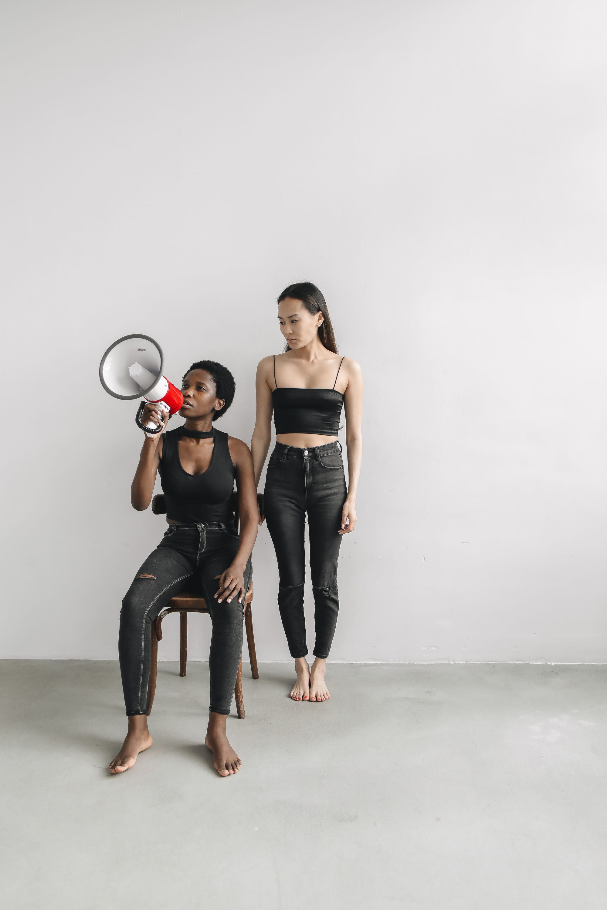 Two women in black outfits posing with a megaphone, expressing empowerment and activism.