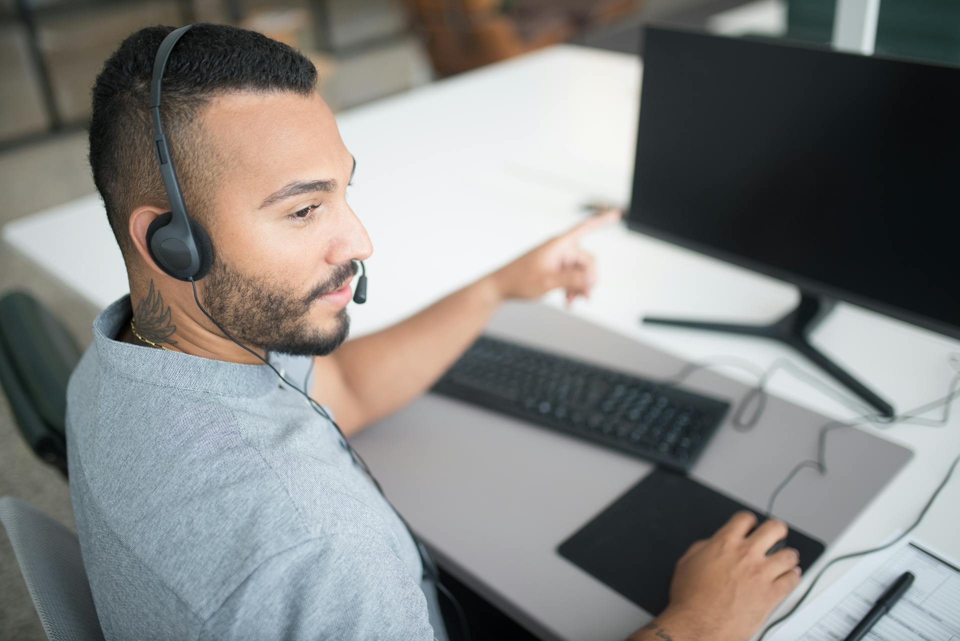 Bearded Man in Gray Shirt Wearing Black Headset Using Computer