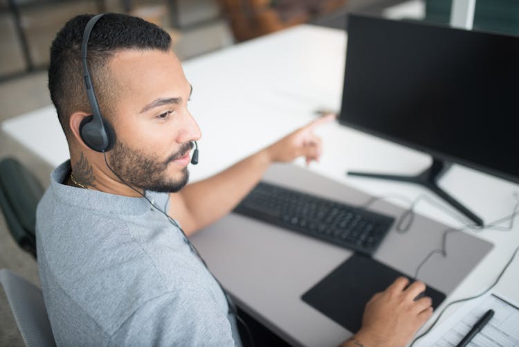 Bearded Man In Gray Shirt Wearing Black Headset Using Computer