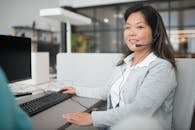 Smiling Woman in Gray Long Sleeve Shirt Sitting in Front of a Desktop Computer