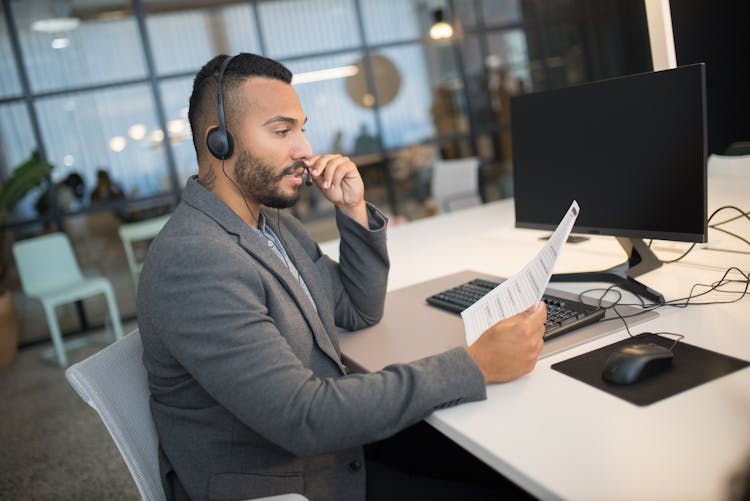 Man In Gray Coat Holding A Paper And Talking On Headset 