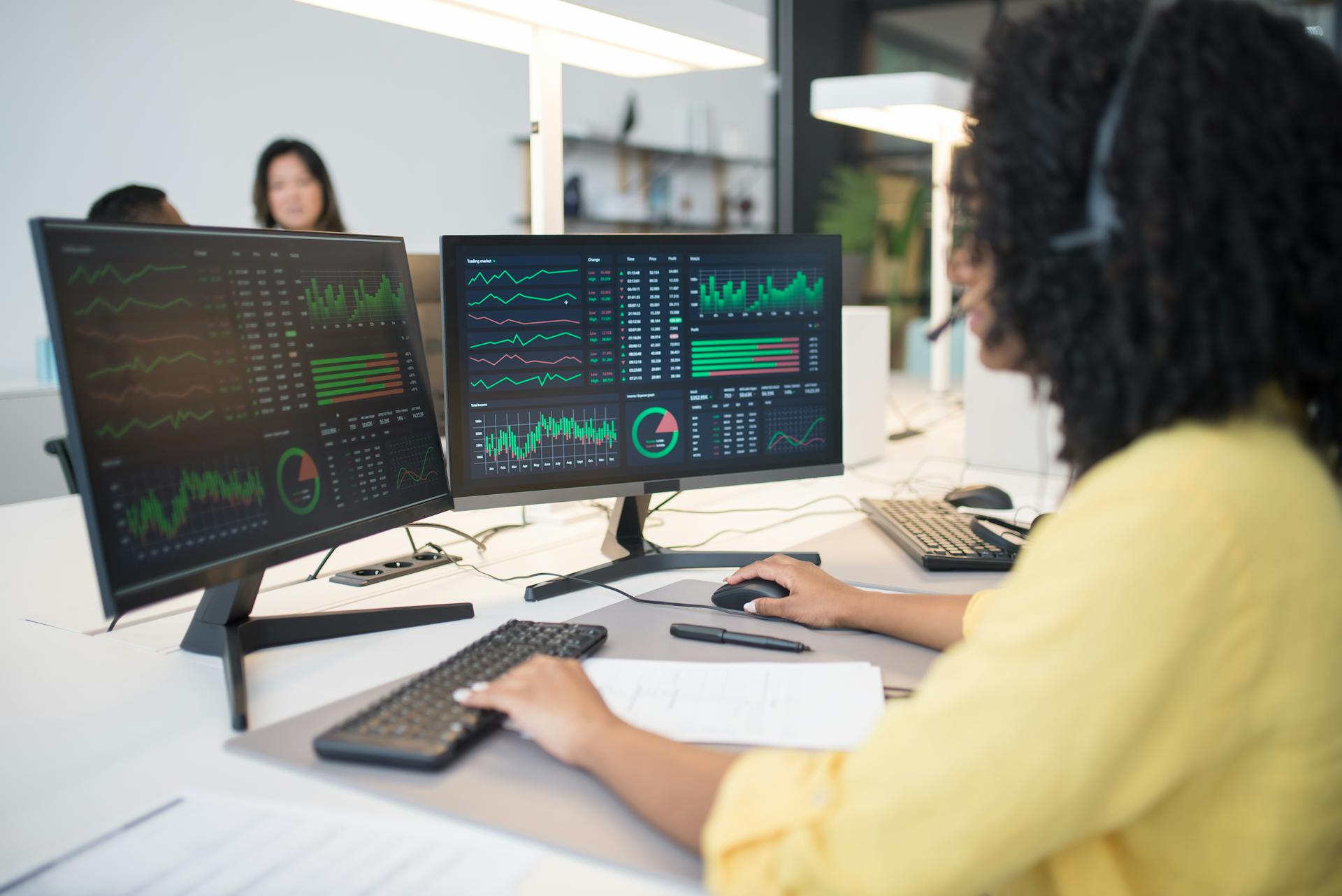 Woman analyzing financial data on dual screens at an office desk.