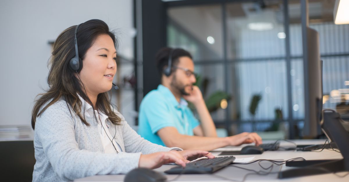 Two professionals with headsets working at computers in a modern office setting.
