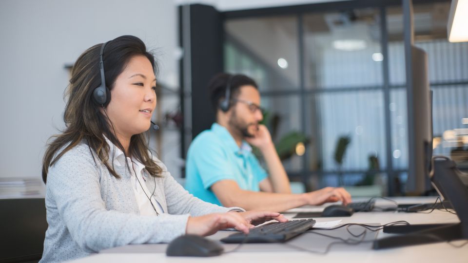 Support agents wearing headsets working side by side at computers in an office.