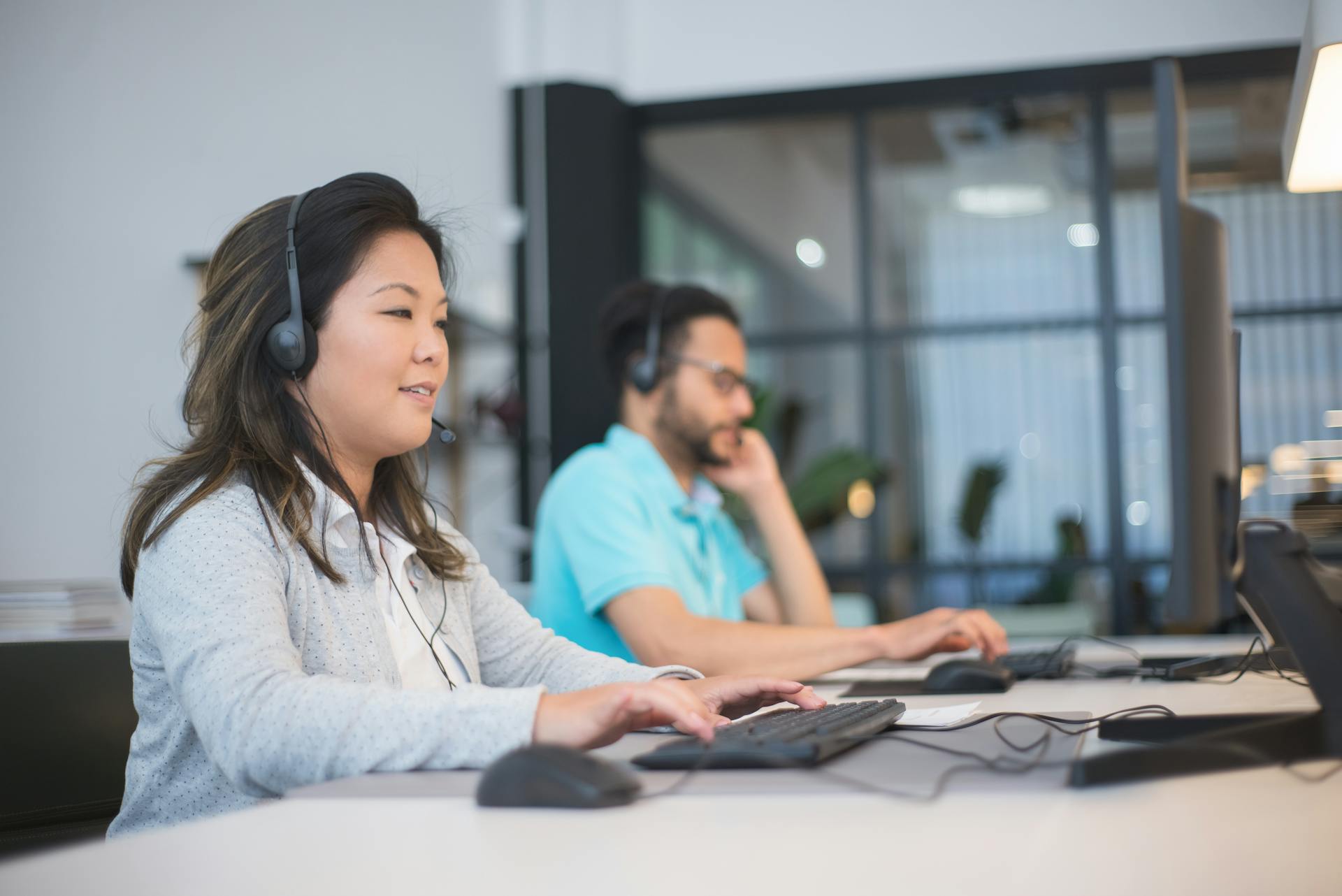 Two professionals with headsets working at computers in a modern office setting.