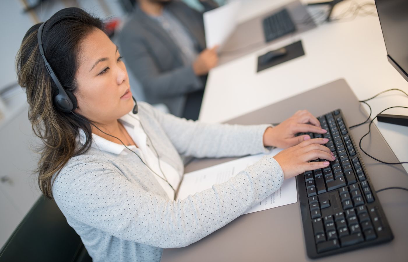 Asian woman working at a computer with headphones in a modern office setting.