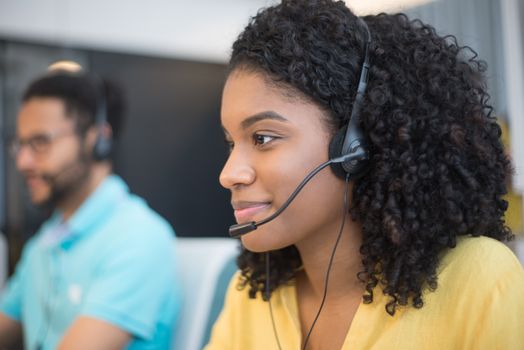 Close-up of an African American woman with curly hair working at a call center, wearing a headset.
