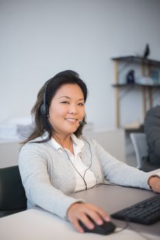 Asian woman working at a call center with a headset in an office setting.