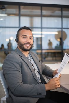 Business professional in office wearing headset and smiling while holding a document.