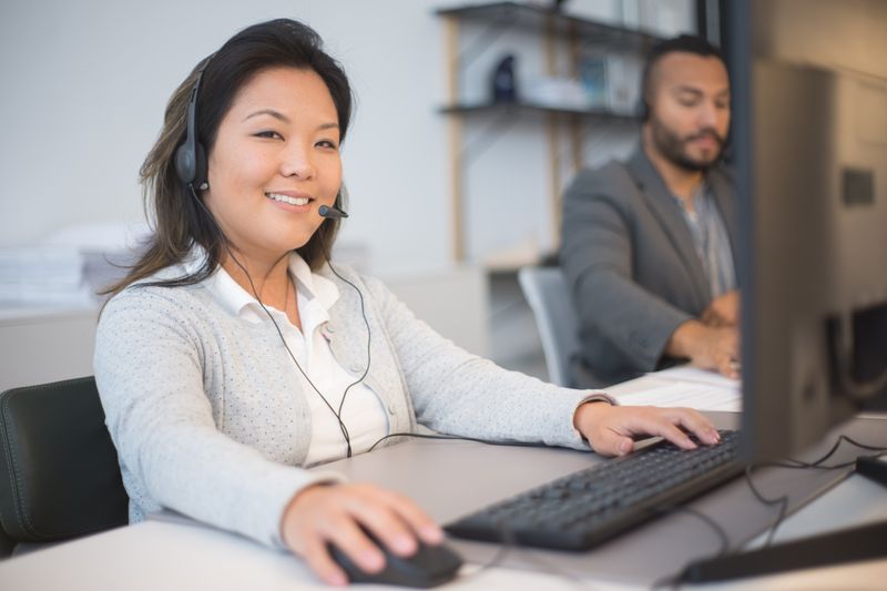 Two call center employees working with headsets in a modern office setting.