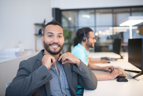 Free Two men in modern office setting with computers, headsets, and smiles, enhancing productivity. Stock Photo