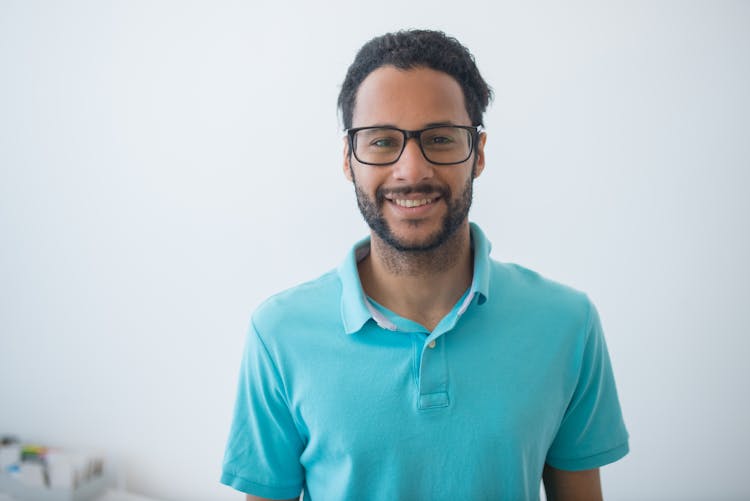 Close-Up Shot Of A Man In Blue Polo Shirt Wearing Eyeglasses On White Surface