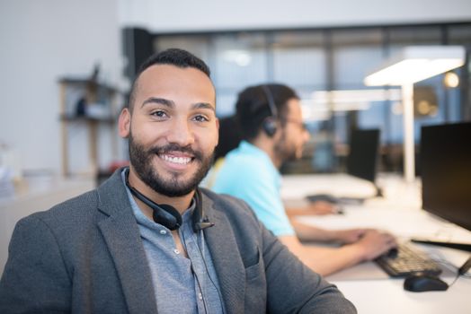 Close-up of a smiling man with a headset in a modern office setting.
