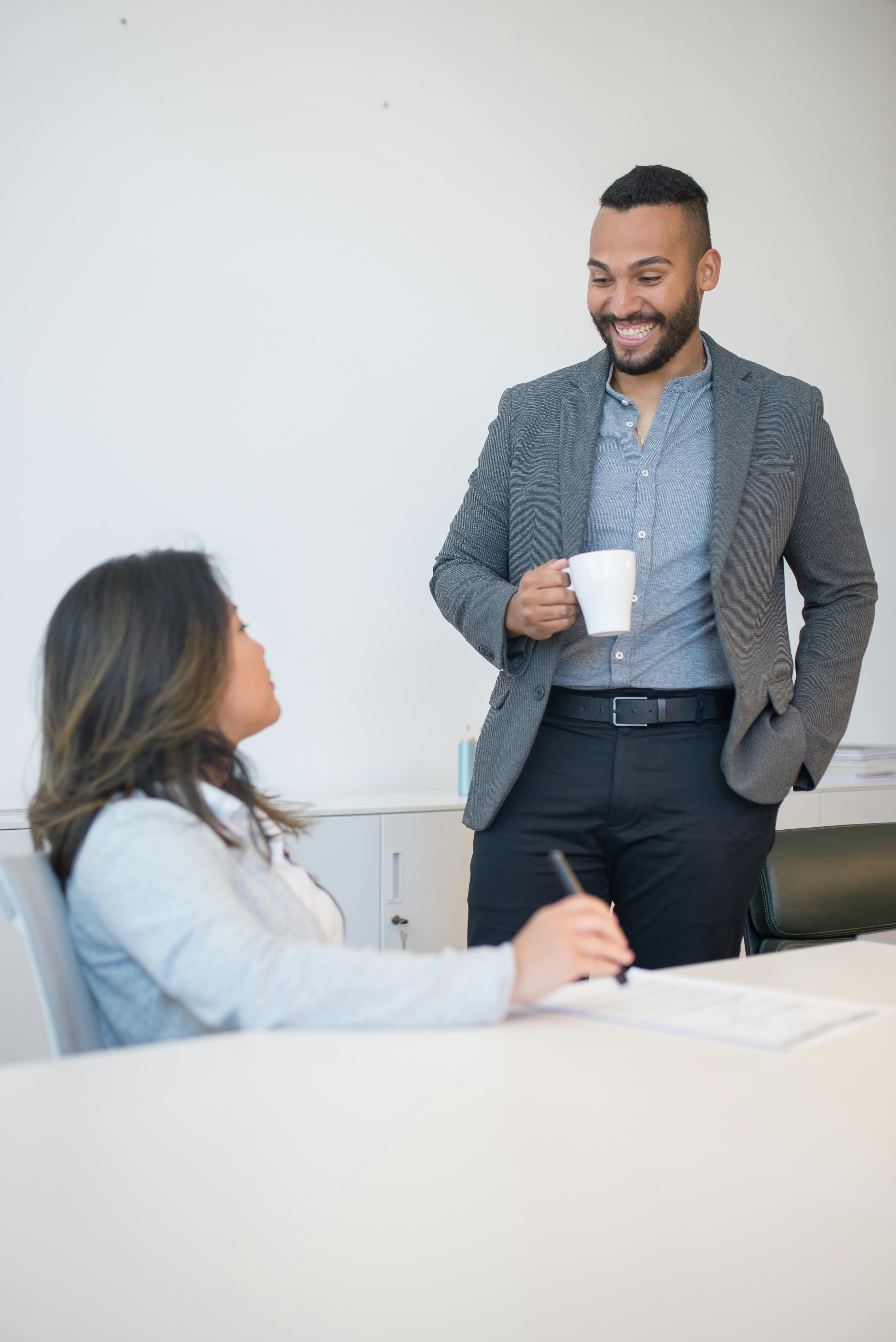 Smiling professional colleagues in a modern office sharing a coffee break discussion.