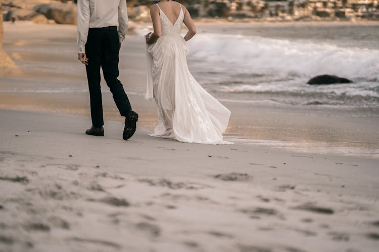 Back View Shot Of Newlywed Couple Walking On The Beach