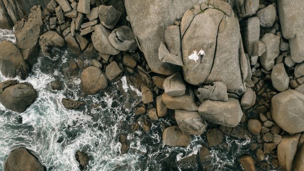 Aerial view of a couple in love on rugged ocean rocks, showcasing nature's beauty.