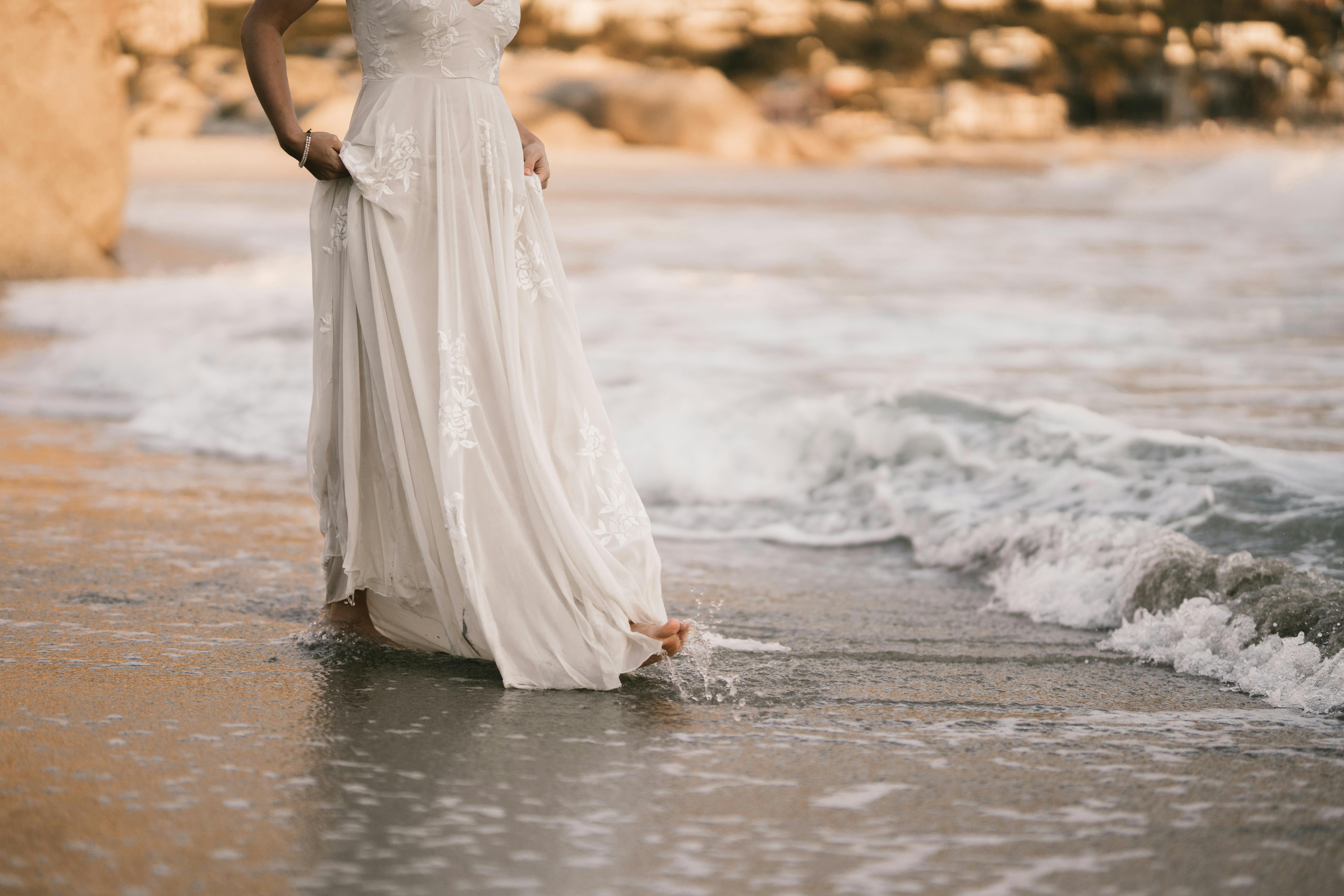 woman in white wedding dress walking on seashore