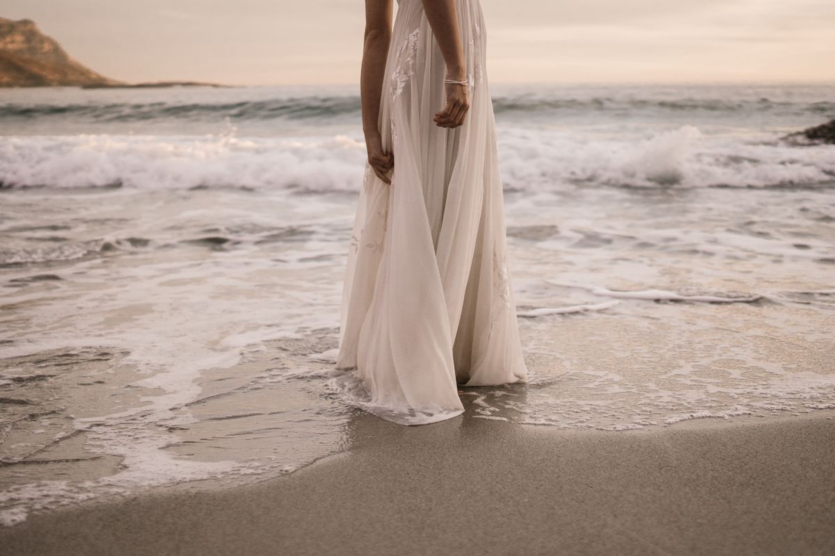 Bride in white wedding dress standing on beach at sunset — bridal anklet styling