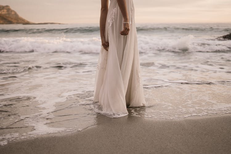 Woman In White Long Dress Standing On Beach