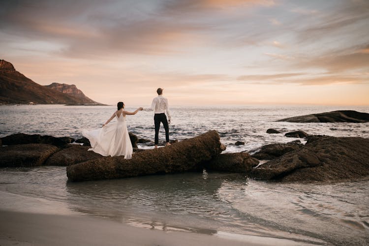 Couple Standing On Rock In Beach During Sunset