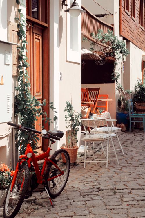 Free Red bicycle parked on charming cobblestone alley with outdoor cafe seating Stock Photo