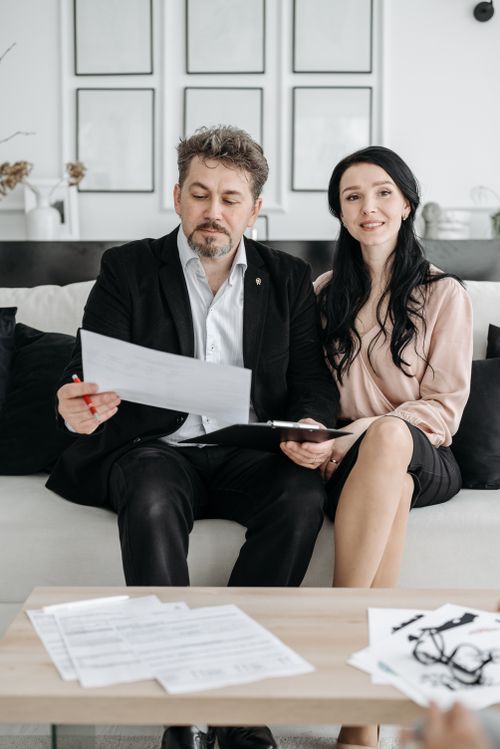 Free A couple is sitting on a sofa reviewing documents together in a modern living room. Stock Photo
