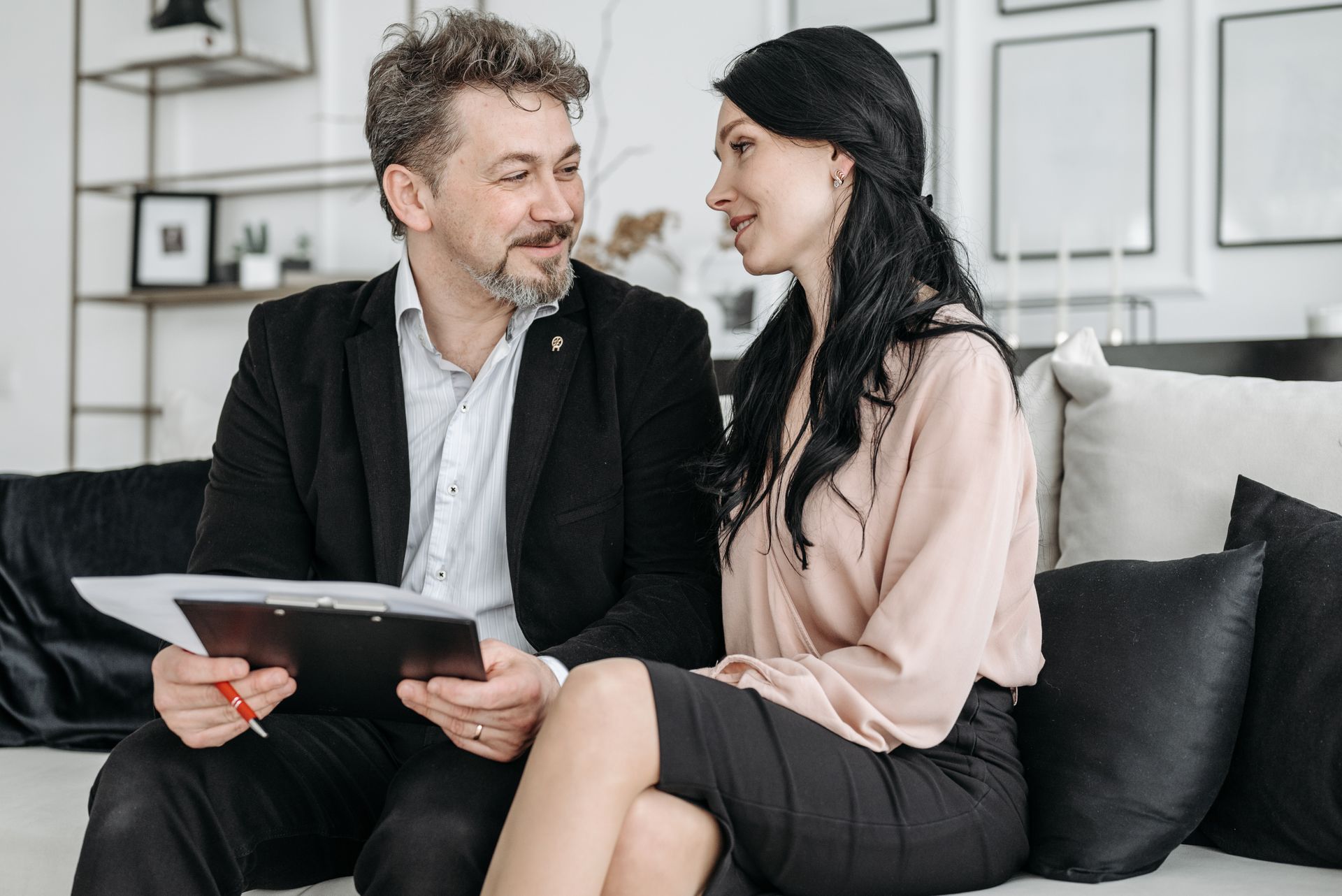 A couple sitting on a couch, smiling, and reviewing documents indoors.