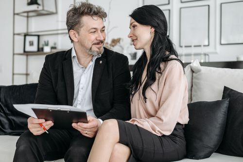 Free A couple sitting on a couch, smiling, and reviewing documents indoors. Stock Photo