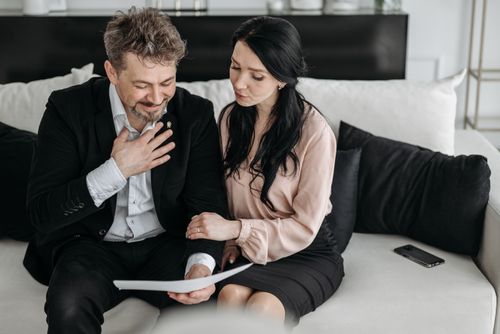Free A joyful couple sitting on a sofa, looking at paperwork, signifying success or good news. Stock Photo