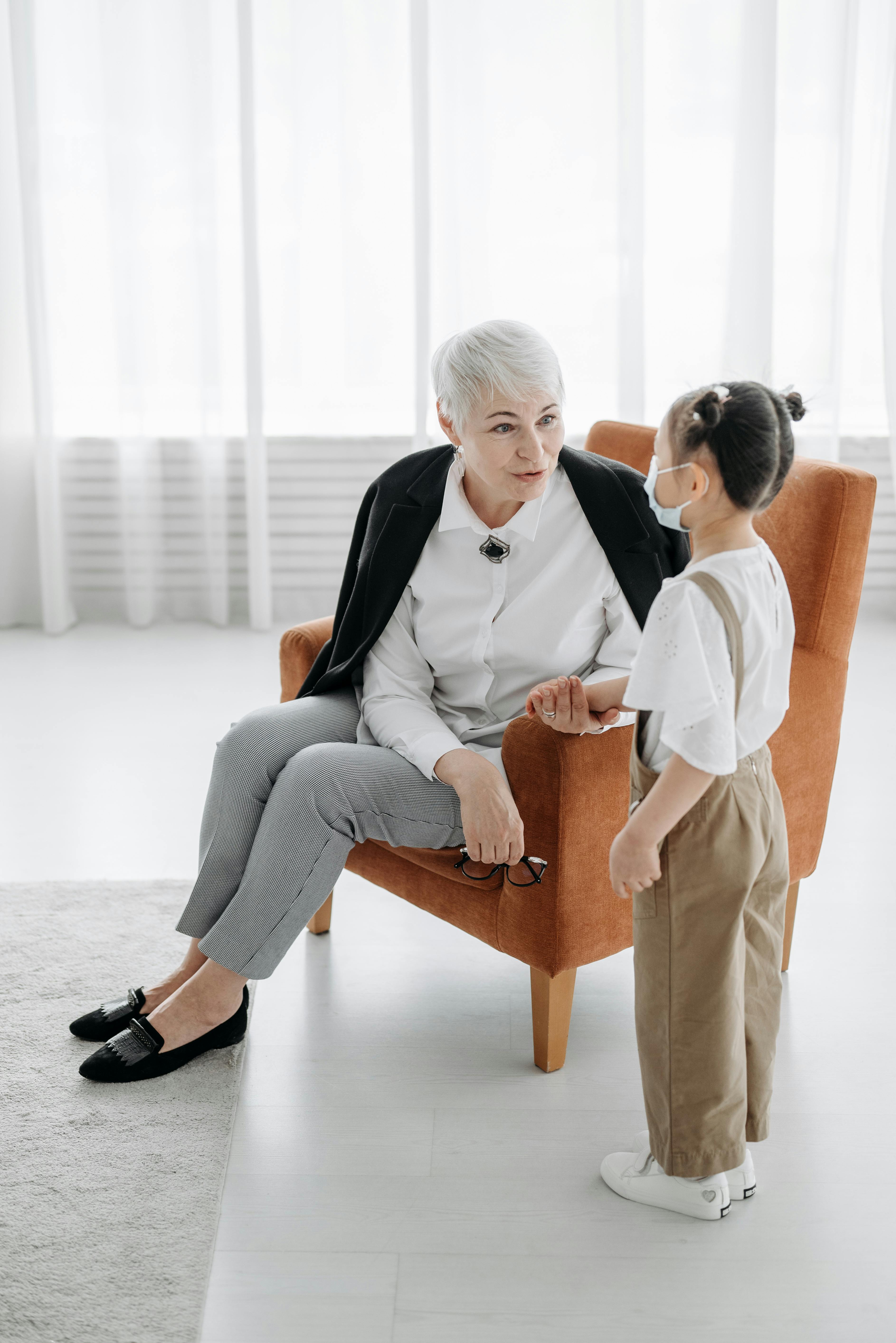 A social worker communicates with a child wearing a mask in a well-lit room.