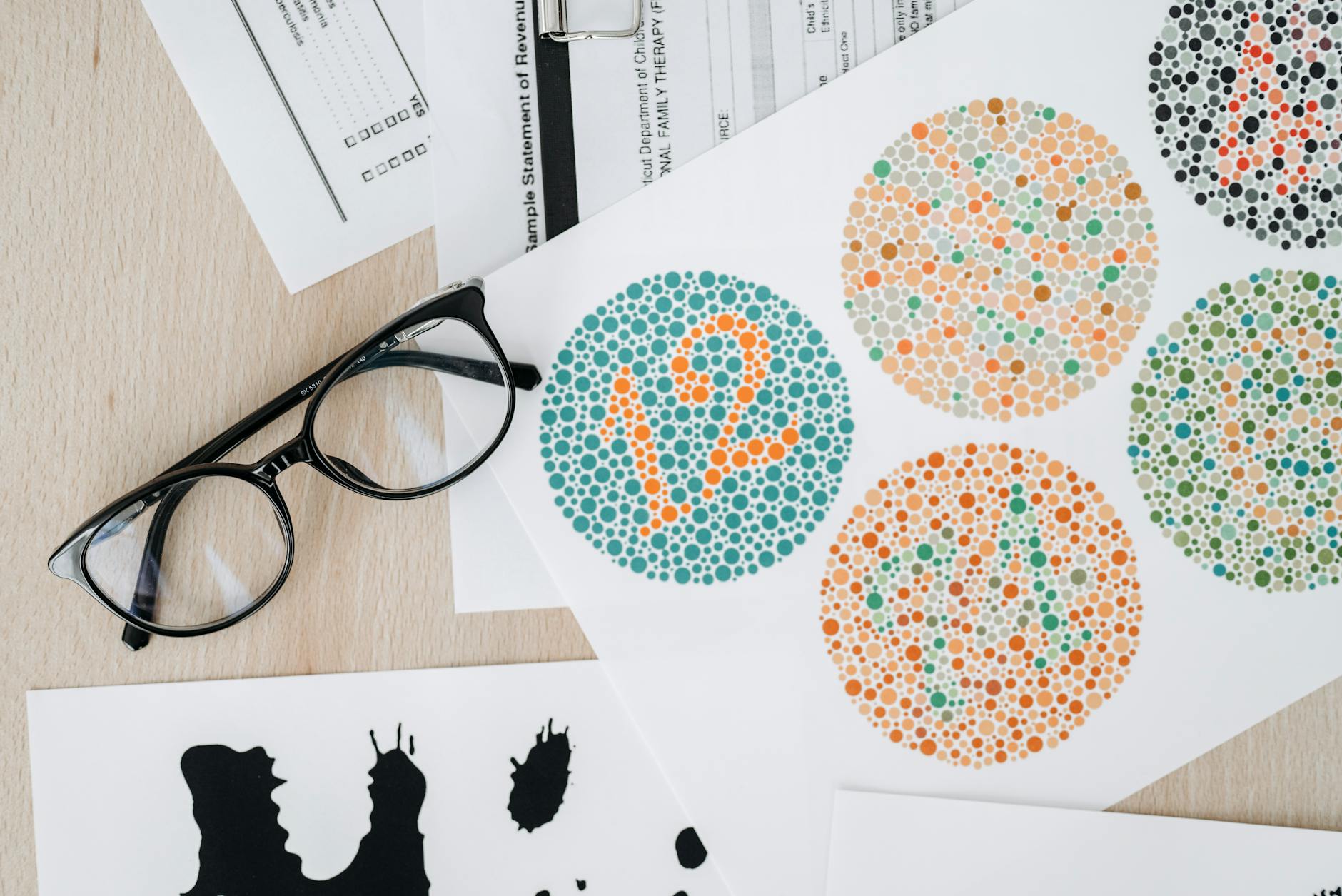 Close-up of color blindness test sheets with eyeglasses on a wooden table.