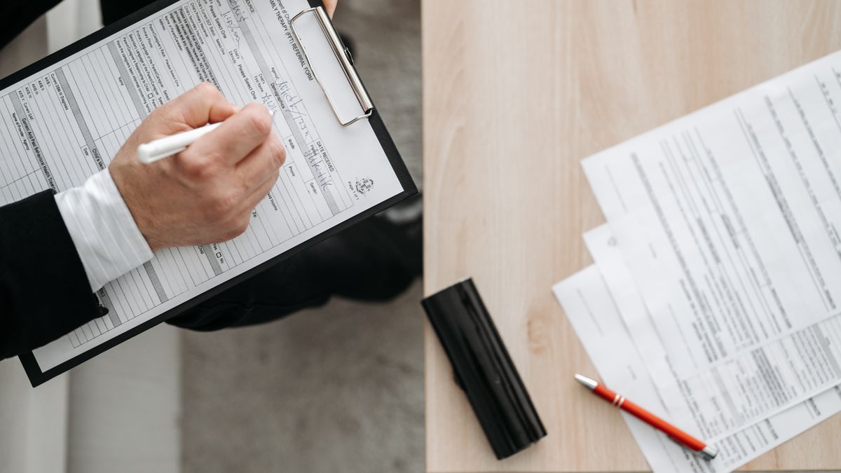 High-angle view of a person filling out forms on a clipboard, emphasizing paperwork and documentation.