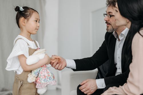 Free A joyful moment of a couple adopting a young Asian girl holding a teddy bear indoors. Stock Photo