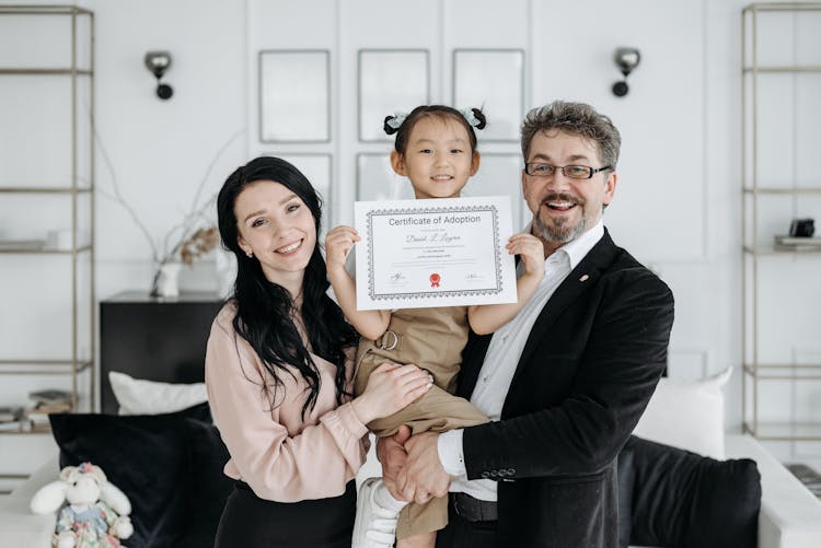 A Couple Carrying A Girl Holding An Adoption Certificate