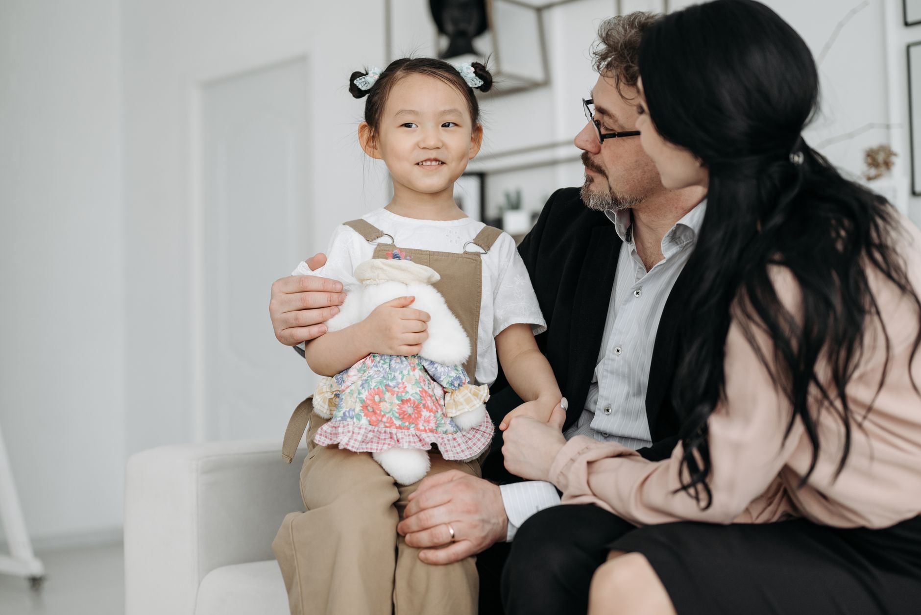 A joyful family scene with adopted child cuddling a stuffed toy indoor setting.
