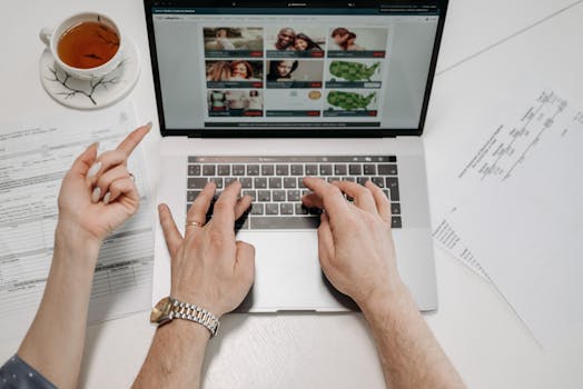 A close-up view of hands typing on a laptop with documents and tea on a desk suggests professionalism and focus.