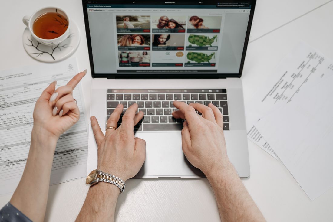 A writer's hands typing on a laptop beside a cup of tea