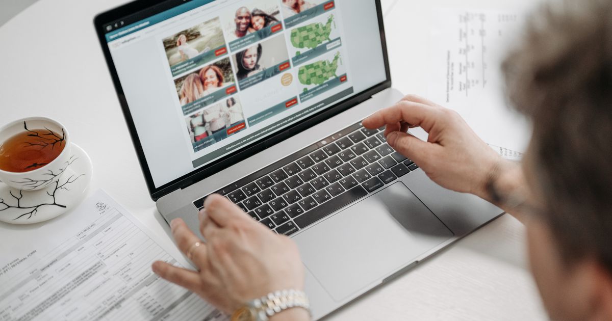 Person browsing a website on a laptop beside a cup of tea and paperwork