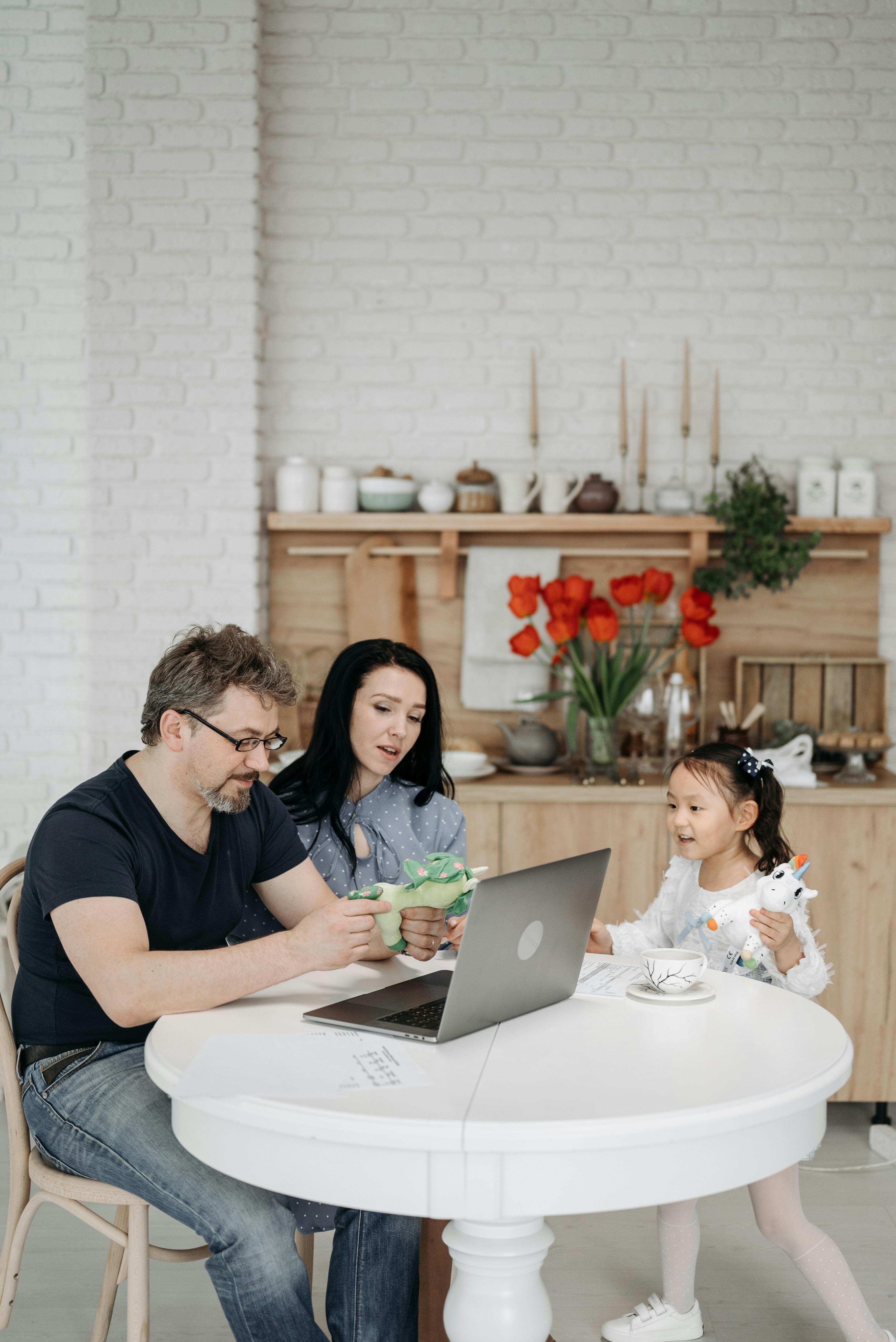 family with a little daughter sitting at the table and looking at a laptop screen