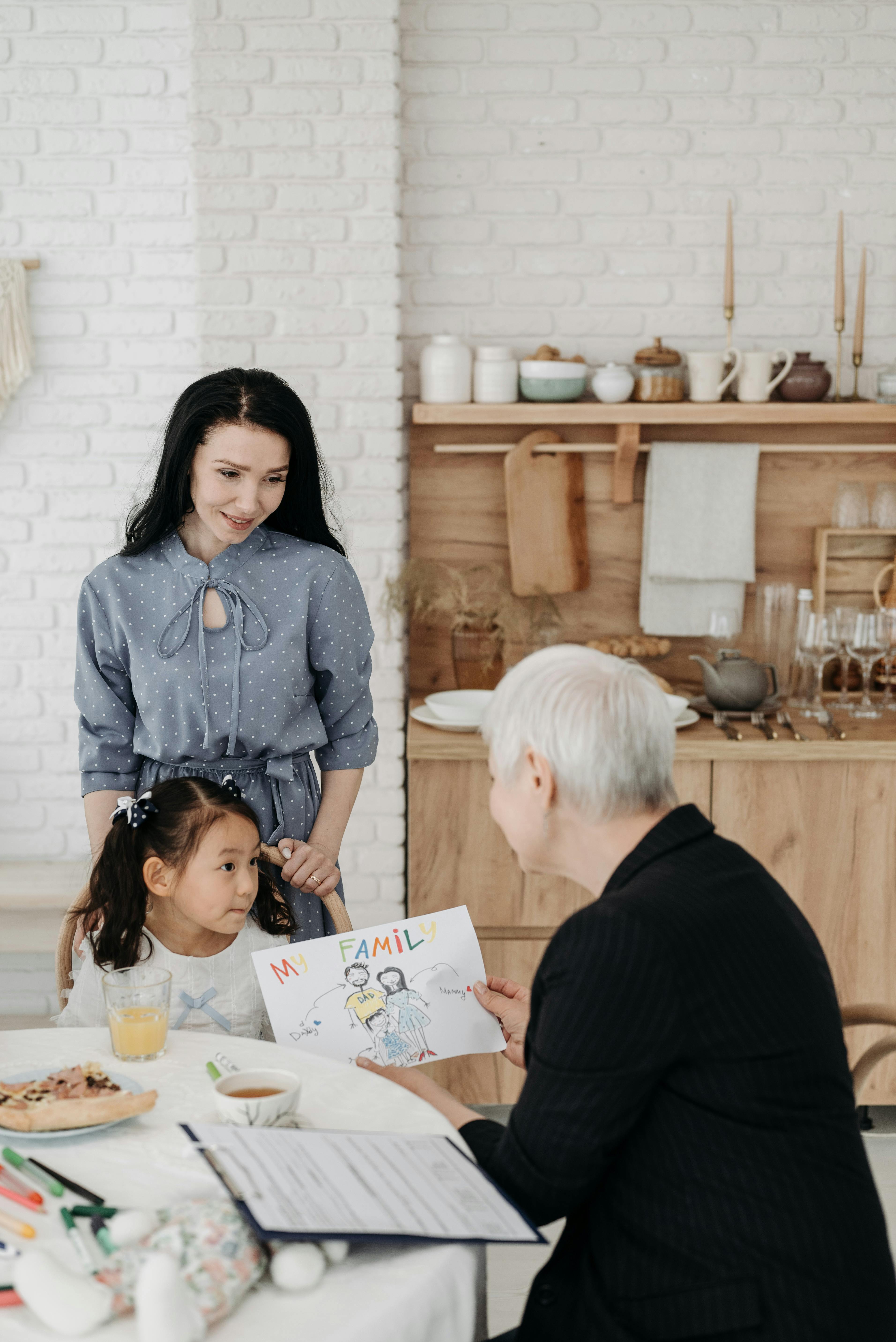 A girl shows her family drawing to two adults in a cozy kitchen, symbolizing love and togetherness.