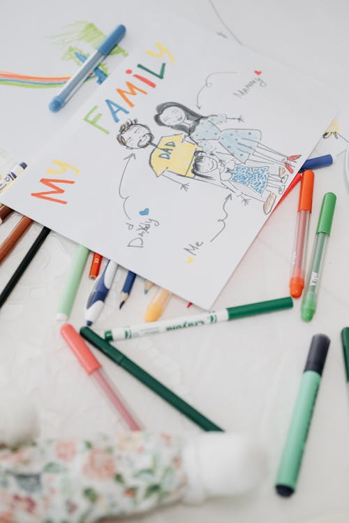 Childs Drawing of a Family and Colorful Pens Lying on the Table 