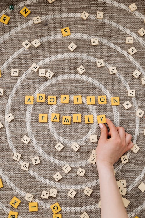 Top View of a Person Making Words Out of Tiles with Letters Saying "Adoption Family"