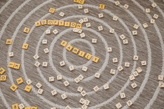 Scrabble tiles spell 'adoption' and 'family' on a textured carpet background, symbolizing family unity.
