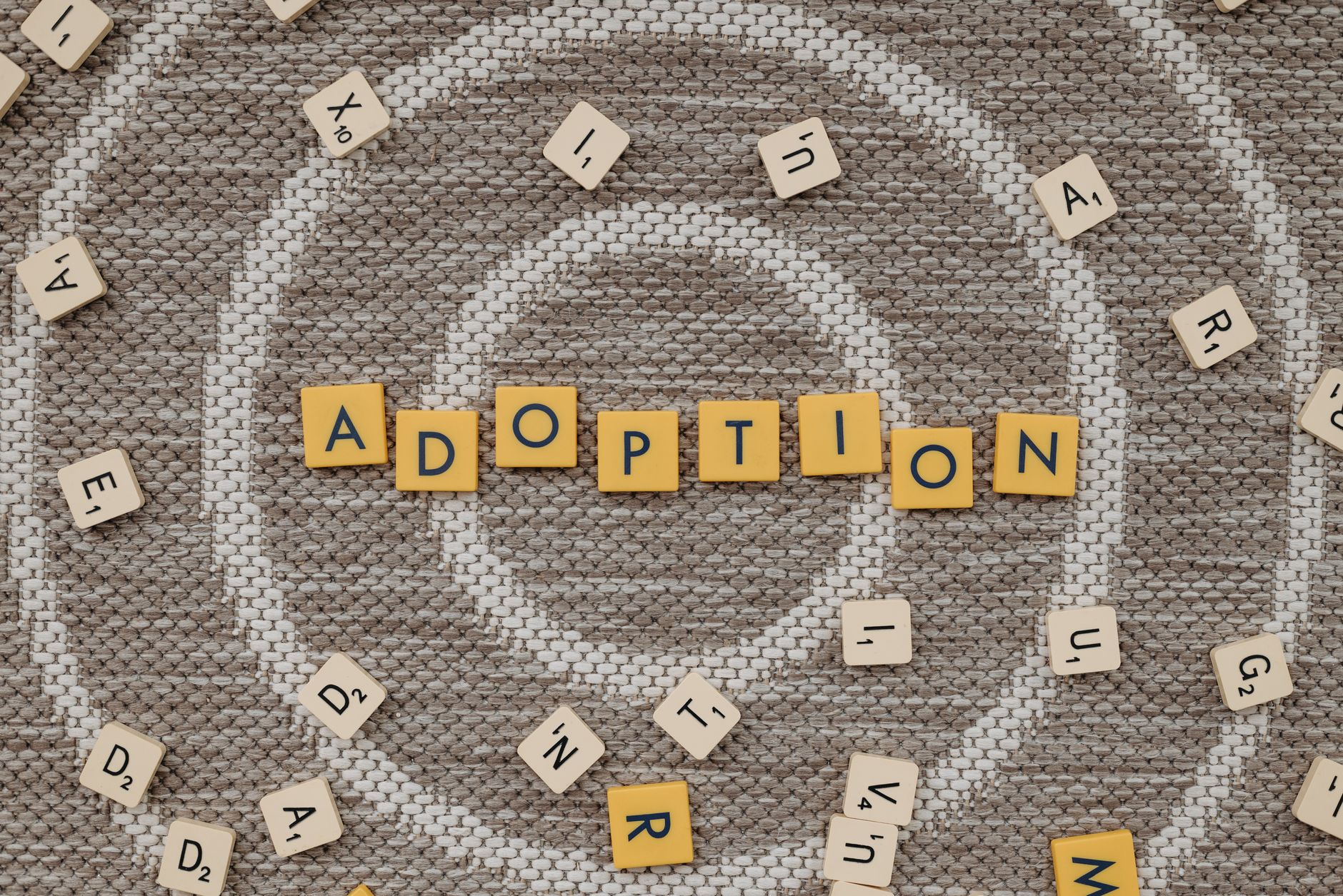 Top view of scrabble letters spelling 'adoption' surrounded by random letters on a patterned surface.