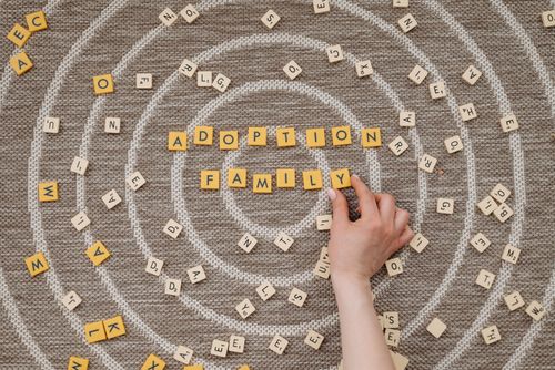 Free Hand arranging scrabble tiles to spell adoption and family on a circular patterned background. Stock Photo