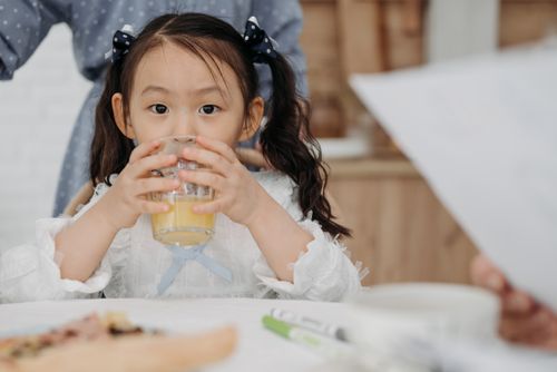 Free A young girl drinking orange juice while sitting at a table indoors, showcasing a cozy family atmosphere. Stock Photo
