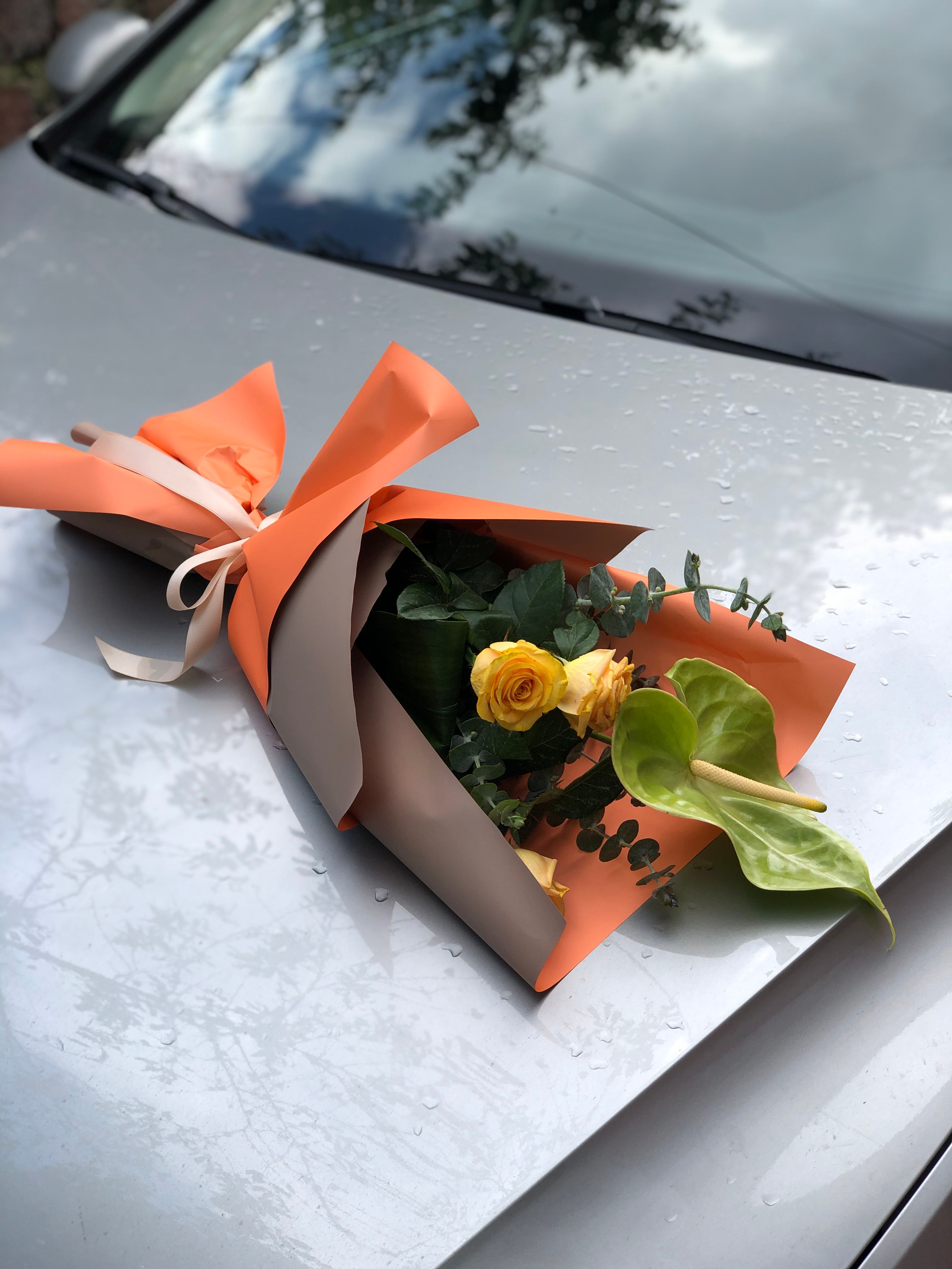 Elegant yellow rose bouquet with anthurium on a car hood, perfect for romantic occasions.