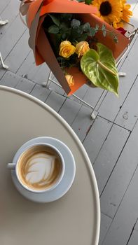 A stylish cup of coffee with a bouquet of roses and sunflowers on a table in Fatih, Istanbul.