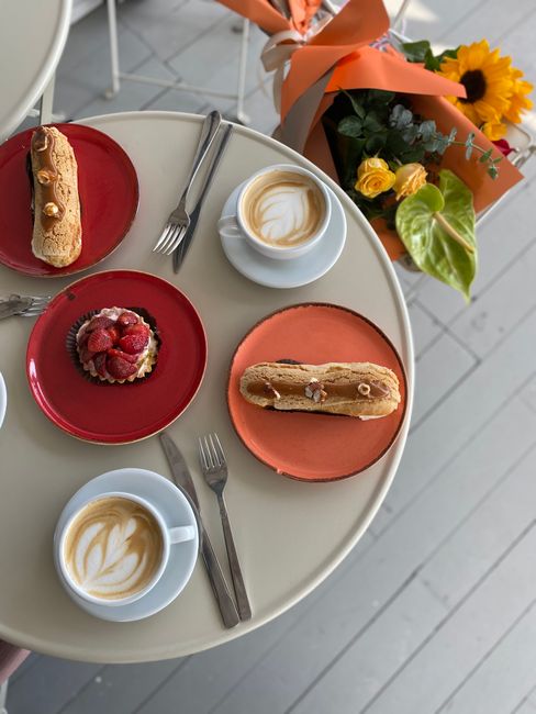 Top view of coffee and desserts on a table with bouquet of flowers.